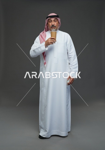 رجل  عربي سعودي خليجي مسن يرتدي الزي الثوب الابيض والشماغ ويحمل فنجان قهوة,  ايماءات واشارات مختلفه , كامل الجسم, خلفيه رماديه
