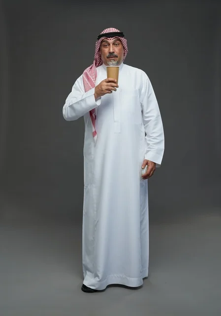 رجل  عربي سعودي خليجي مسن يرتدي الزي الثوب الابيض والشماغ ويحمل فنجان قهوة,  ايماءات واشارات مختلفه , كامل الجسم, خلفيه رماديه