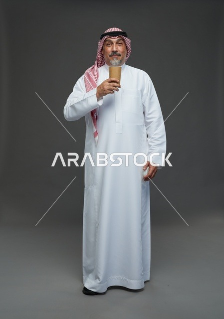 رجل  عربي سعودي خليجي مسن يرتدي الزي الثوب الابيض والشماغ ويحمل فنجان قهوة,  ايماءات واشارات مختلفه , كامل الجسم, خلفيه رماديه