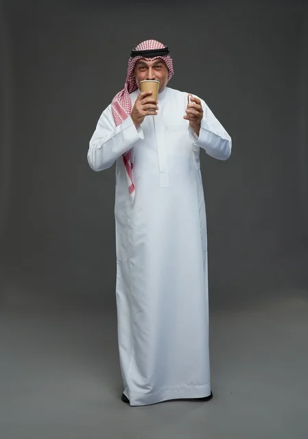 An elderly Arab Saudi Gulf man wearing a white thobe and a shemagh, holding a cup of coffee, with various gestures and signs, full body, gray background.