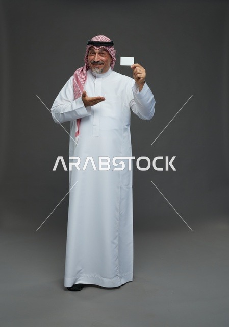 رجل  عربي سعودي خليجي مسن يرتدي الزي الثوب الابيض والشماغ ويمسك بطاقه بيضاء فارغه,  ايماءات واشارات مختلفه , كامل الجسم, خلفيه رماديه