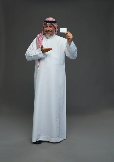 رجل  عربي سعودي خليجي مسن يرتدي الزي الثوب الابيض والشماغ ويمسك بطاقه بيضاء فارغه,  ايماءات واشارات مختلفه , كامل الجسم, خلفيه رماديه