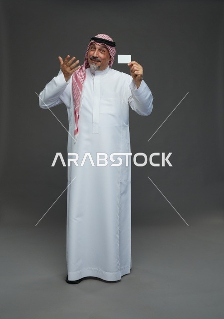رجل  عربي سعودي خليجي مسن يرتدي الزي الثوب الابيض والشماغ ويمسك بطاقه بيضاء فارغه,  ايماءات واشارات مختلفه , كامل الجسم, خلفيه رماديه