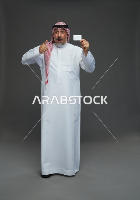 رجل  عربي سعودي خليجي مسن يرتدي الزي الثوب الابيض والشماغ ويمسك بطاقه بيضاء فارغه,  ايماءات واشارات مختلفه , كامل الجسم, خلفيه رماديه