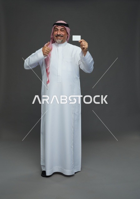 رجل  عربي سعودي خليجي مسن يرتدي الزي الثوب الابيض والشماغ ويمسك بطاقه بيضاء فارغه,  ايماءات واشارات مختلفه , كامل الجسم, خلفيه رماديه