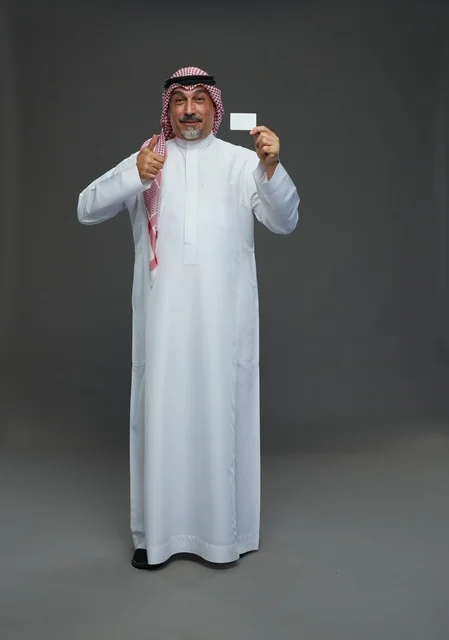 رجل  عربي سعودي خليجي مسن يرتدي الزي الثوب الابيض والشماغ ويمسك بطاقه بيضاء فارغه,  ايماءات واشارات مختلفه , كامل الجسم, خلفيه رماديه