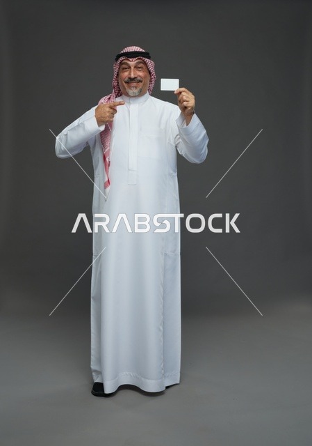 رجل  عربي سعودي خليجي مسن يرتدي الزي الثوب الابيض والشماغ ويمسك بطاقه بيضاء فارغه,  ايماءات واشارات مختلفه , كامل الجسم, خلفيه رماديه