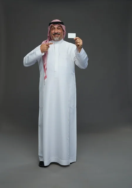 رجل  عربي سعودي خليجي مسن يرتدي الزي الثوب الابيض والشماغ ويمسك بطاقه بيضاء فارغه,  ايماءات واشارات مختلفه , كامل الجسم, خلفيه رماديه