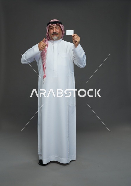 رجل  عربي سعودي خليجي مسن يرتدي الزي الثوب الابيض والشماغ ويمسك بطاقه بيضاء فارغه,  ايماءات واشارات مختلفه , كامل الجسم, خلفيه رماديه