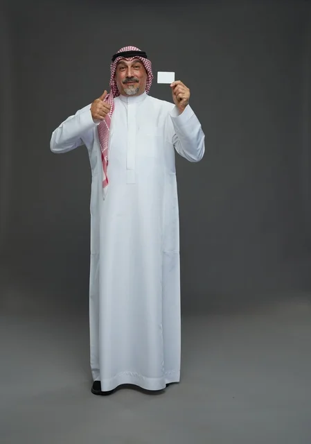 رجل  عربي سعودي خليجي مسن يرتدي الزي الثوب الابيض والشماغ ويمسك بطاقه بيضاء فارغه,  ايماءات واشارات مختلفه , كامل الجسم, خلفيه رماديه