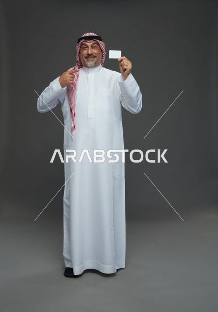 رجل  عربي سعودي خليجي مسن يرتدي الزي الثوب الابيض والشماغ ويمسك بطاقه بيضاء فارغه,  ايماءات واشارات مختلفه , كامل الجسم, خلفيه رماديه