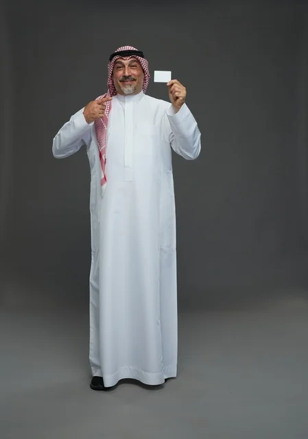 An elderly Arab Saudi Gulf man wearing a white thobe and a shemagh, holding a blank white card, with various gestures and signs, full body, gray background.