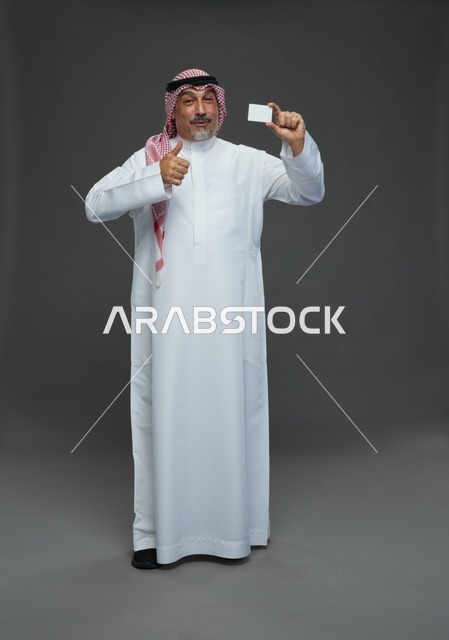 رجل  عربي سعودي خليجي مسن يرتدي الزي الثوب الابيض والشماغ ويمسك بطاقه بيضاء فارغه,  ايماءات واشارات مختلفه , كامل الجسم, خلفيه رماديه
