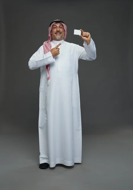 An elderly Arab Saudi Gulf man wearing a white thobe and a shemagh, holding a blank white card, with various gestures and signs, full body, gray background.