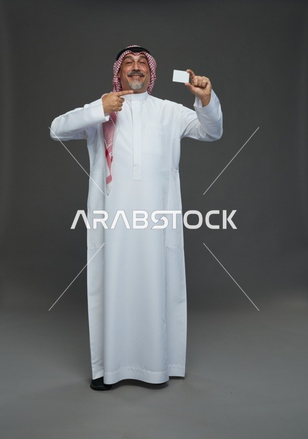 رجل  عربي سعودي خليجي مسن يرتدي الزي الثوب الابيض والشماغ ويمسك بطاقه بيضاء فارغه,  ايماءات واشارات مختلفه , كامل الجسم, خلفيه رماديه