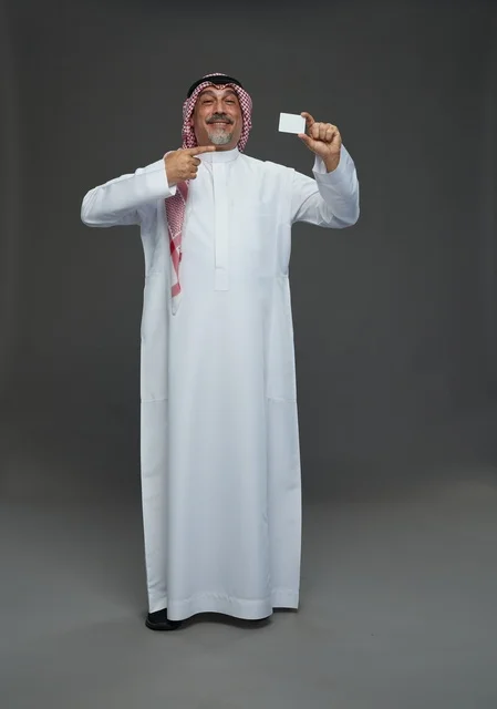 رجل  عربي سعودي خليجي مسن يرتدي الزي الثوب الابيض والشماغ ويمسك بطاقه بيضاء فارغه,  ايماءات واشارات مختلفه , كامل الجسم, خلفيه رماديه