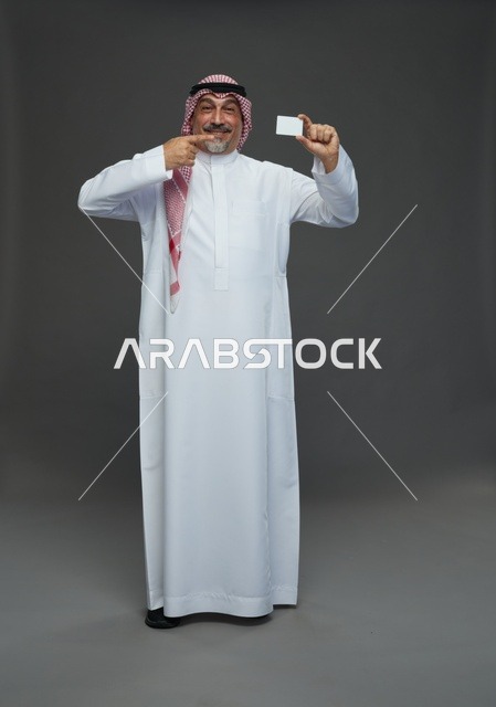 رجل  عربي سعودي خليجي مسن يرتدي الزي الثوب الابيض والشماغ ويمسك بطاقه بيضاء فارغه,  ايماءات واشارات مختلفه , كامل الجسم, خلفيه رماديه