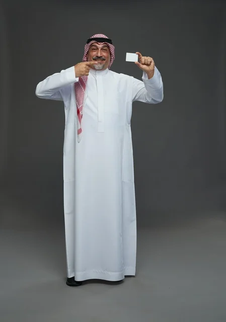 رجل  عربي سعودي خليجي مسن يرتدي الزي الثوب الابيض والشماغ ويمسك بطاقه بيضاء فارغه,  ايماءات واشارات مختلفه , كامل الجسم, خلفيه رماديه