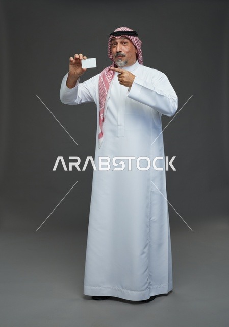 رجل  عربي سعودي خليجي مسن يرتدي الزي الثوب الابيض والشماغ ويمسك بطاقه بيضاء فارغه,  ايماءات واشارات مختلفه , كامل الجسم, خلفيه رماديه