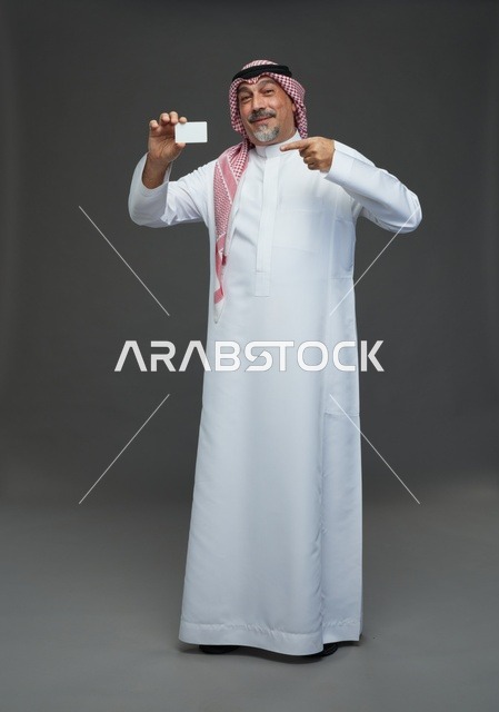 رجل  عربي سعودي خليجي مسن يرتدي الزي الثوب الابيض والشماغ ويمسك بطاقه بيضاء فارغه,  ايماءات واشارات مختلفه , كامل الجسم, خلفيه رماديه