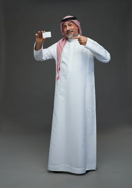 رجل  عربي سعودي خليجي مسن يرتدي الزي الثوب الابيض والشماغ ويمسك بطاقه بيضاء فارغه,  ايماءات واشارات مختلفه , كامل الجسم, خلفيه رماديه