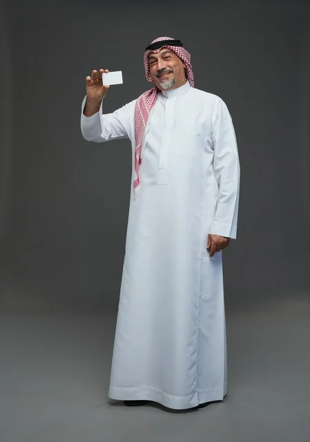 رجل  عربي سعودي خليجي مسن يرتدي الزي الثوب الابيض والشماغ ويمسك بطاقه بيضاء فارغه,  ايماءات واشارات مختلفه , كامل الجسم, خلفيه رماديه
