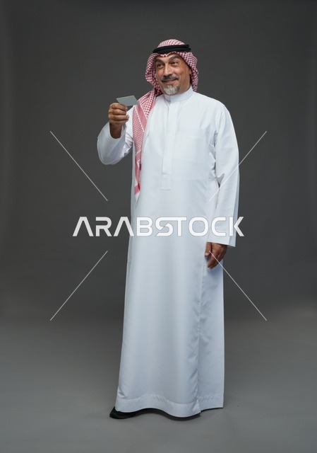 An elderly Arab Saudi Gulf man wearing a white thobe and a shemagh, holding a blank white card, with various gestures and signs, full body, gray background.