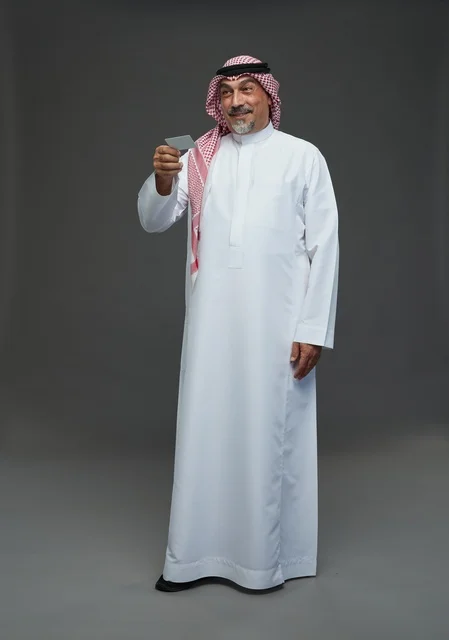 رجل  عربي سعودي خليجي مسن يرتدي الزي الثوب الابيض والشماغ ويمسك بطاقه بيضاء فارغه,  ايماءات واشارات مختلفه , كامل الجسم, خلفيه رماديه