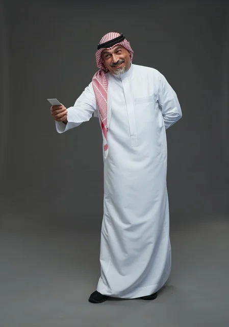 رجل  عربي سعودي خليجي مسن يرتدي الزي الثوب الابيض والشماغ ويمسك بطاقه بيضاء فارغه,  ايماءات واشارات مختلفه , كامل الجسم, خلفيه رماديه