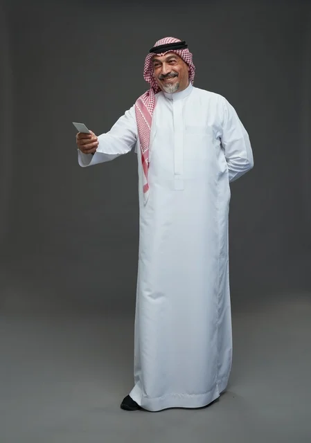 An elderly Arab Saudi Gulf man wearing a white thobe and a shemagh, holding a blank white card, with various gestures and signs, full body, gray background.