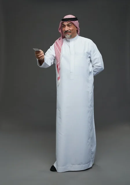 An elderly Arab Saudi Gulf man wearing a white thobe and a shemagh, holding a blank white card, with various gestures and signs, full body, gray background.