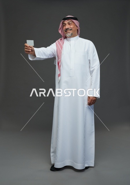 رجل  عربي سعودي خليجي مسن يرتدي الزي الثوب الابيض والشماغ ويمسك بطاقه بيضاء فارغه,  ايماءات واشارات مختلفه , كامل الجسم, خلفيه رماديه