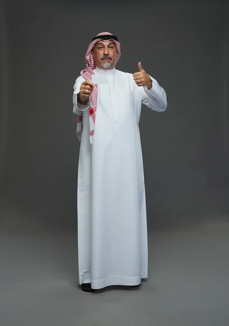An elderly Arab Saudi Gulf man wearing a white thobe and a shemagh, holding a blank white card, with various gestures and signs, full body, gray background.