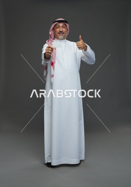 رجل  عربي سعودي خليجي مسن يرتدي الزي الثوب الابيض والشماغ ويمسك بطاقه بيضاء فارغه,  ايماءات واشارات مختلفه , كامل الجسم, خلفيه رماديه