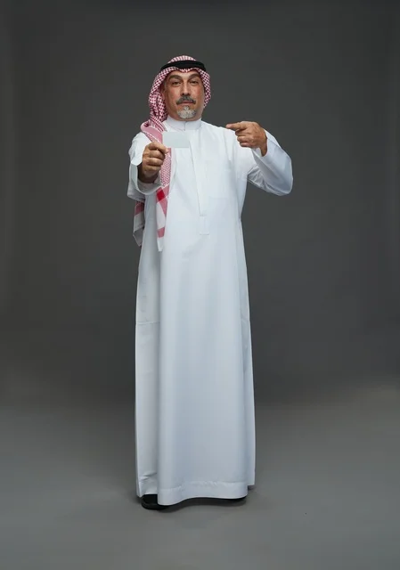 رجل  عربي سعودي خليجي مسن يرتدي الزي الثوب الابيض والشماغ ويمسك بطاقه بيضاء فارغه,  ايماءات واشارات مختلفه , كامل الجسم, خلفيه رماديه