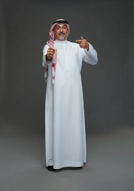 رجل  عربي سعودي خليجي مسن يرتدي الزي الثوب الابيض والشماغ ويمسك بطاقه بيضاء فارغه,  ايماءات واشارات مختلفه , كامل الجسم, خلفيه رماديه