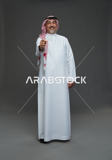رجل  عربي سعودي خليجي مسن يرتدي الزي الثوب الابيض والشماغ ويمسك بطاقه بيضاء فارغه,  ايماءات واشارات مختلفه , كامل الجسم, خلفيه رماديه