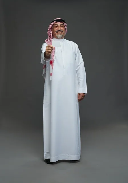 رجل  عربي سعودي خليجي مسن يرتدي الزي الثوب الابيض والشماغ ويمسك بطاقه بيضاء فارغه,  ايماءات واشارات مختلفه , كامل الجسم, خلفيه رماديه