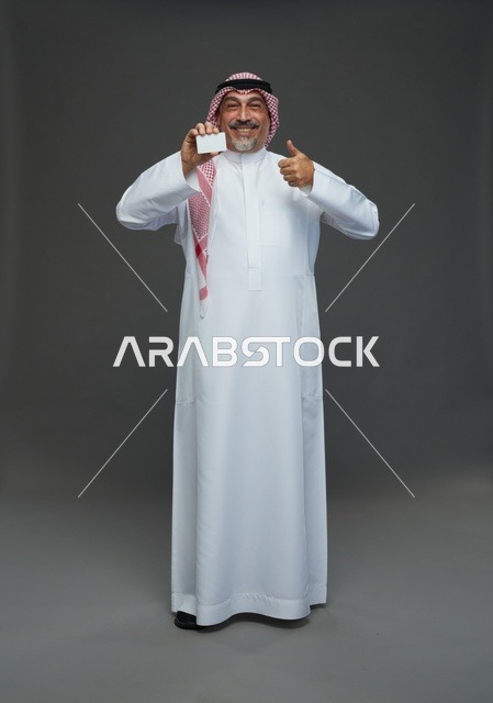 رجل  عربي سعودي خليجي مسن يرتدي الزي الثوب الابيض والشماغ ويمسك بطاقه بيضاء فارغه,  ايماءات واشارات مختلفه , كامل الجسم, خلفيه رماديه