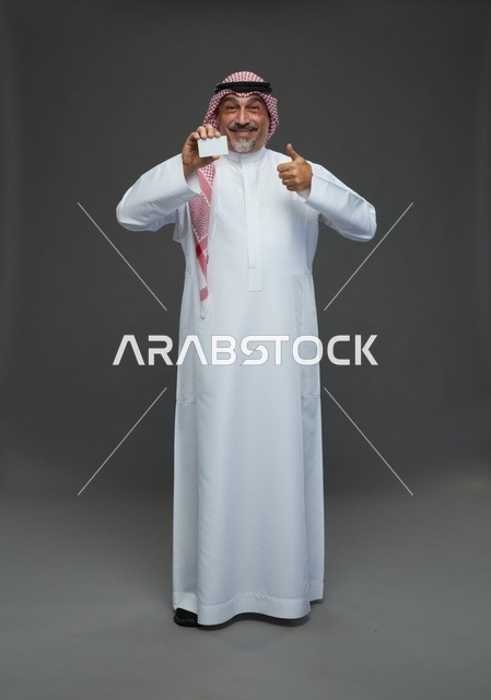 رجل  عربي سعودي خليجي مسن يرتدي الزي الثوب الابيض والشماغ ويمسك بطاقه بيضاء فارغه,  ايماءات واشارات مختلفه , كامل الجسم, خلفيه رماديه