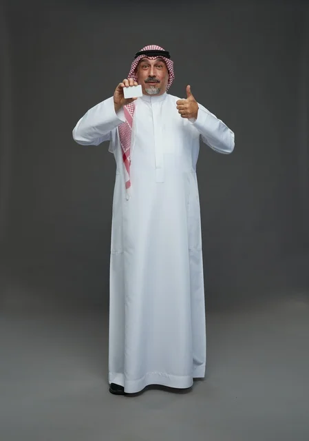 رجل  عربي سعودي خليجي مسن يرتدي الزي الثوب الابيض والشماغ ويمسك بطاقه بيضاء فارغه,  ايماءات واشارات مختلفه , كامل الجسم, خلفيه رماديه