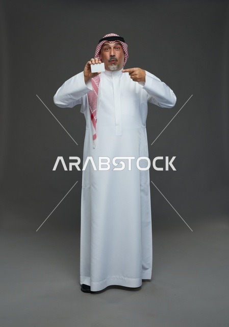 رجل  عربي سعودي خليجي مسن يرتدي الزي الثوب الابيض والشماغ ويمسك بطاقه بيضاء فارغه,  ايماءات واشارات مختلفه , كامل الجسم, خلفيه رماديه