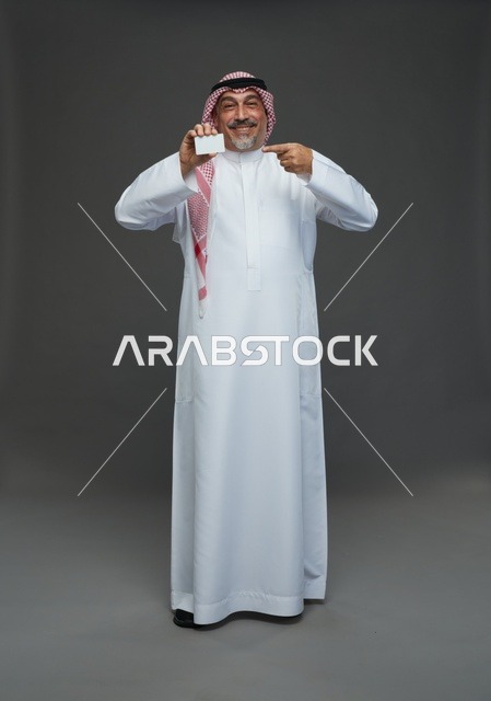 رجل  عربي سعودي خليجي مسن يرتدي الزي الثوب الابيض والشماغ ويمسك بطاقه بيضاء فارغه,  ايماءات واشارات مختلفه , كامل الجسم, خلفيه رماديه