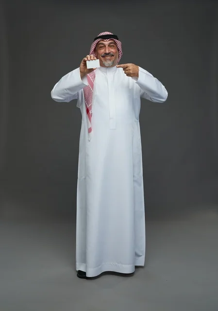 رجل  عربي سعودي خليجي مسن يرتدي الزي الثوب الابيض والشماغ ويمسك بطاقه بيضاء فارغه,  ايماءات واشارات مختلفه , كامل الجسم, خلفيه رماديه
