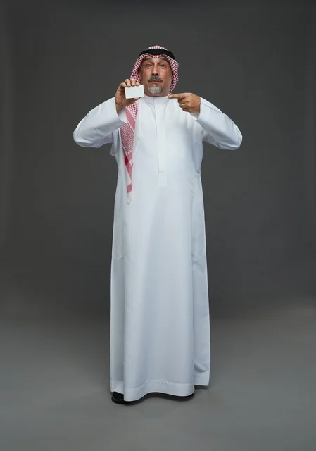 رجل  عربي سعودي خليجي مسن يرتدي الزي الثوب الابيض والشماغ ويمسك بطاقه بيضاء فارغه,  ايماءات واشارات مختلفه , كامل الجسم, خلفيه رماديه