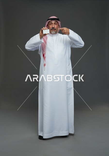 An elderly Arab Saudi Gulf man wearing a white thobe and a shemagh, holding a blank white card, with various gestures and signs, full body, gray background.