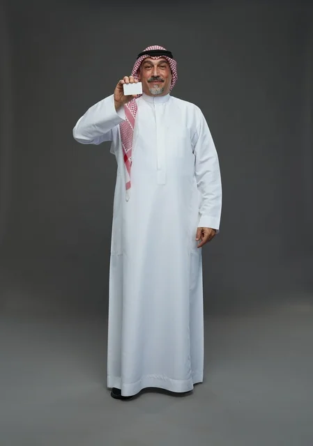 رجل  عربي سعودي خليجي مسن يرتدي الزي الثوب الابيض والشماغ ويمسك بطاقه بيضاء فارغه,  ايماءات واشارات مختلفه , كامل الجسم, خلفيه رماديه