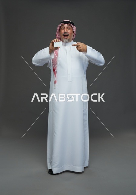 رجل  عربي سعودي خليجي مسن يرتدي الزي الثوب الابيض والشماغ ويمسك بطاقه بيضاء فارغه,  ايماءات واشارات مختلفه , كامل الجسم, خلفيه رماديه