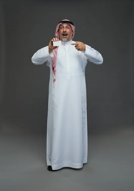 رجل  عربي سعودي خليجي مسن يرتدي الزي الثوب الابيض والشماغ ويمسك بطاقه بيضاء فارغه,  ايماءات واشارات مختلفه , كامل الجسم, خلفيه رماديه