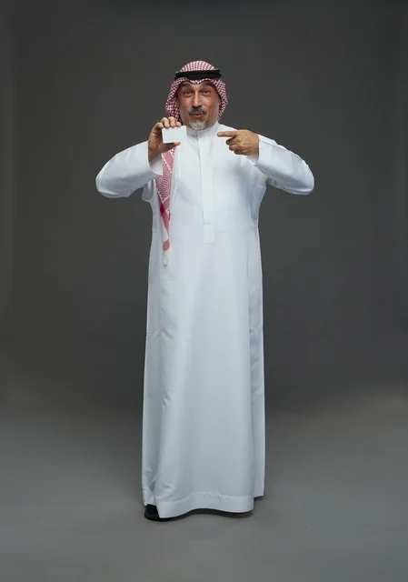 رجل  عربي سعودي خليجي مسن يرتدي الزي الثوب الابيض والشماغ ويمسك بطاقه بيضاء فارغه,  ايماءات واشارات مختلفه , كامل الجسم, خلفيه رماديه